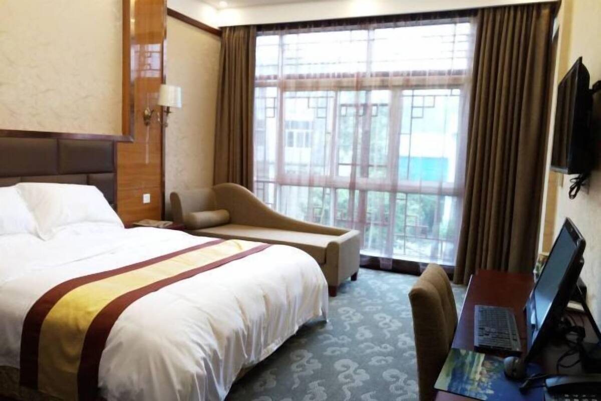 Habitación de hotel con una cama grande, un escritorio con ordenador, una silla y una ventana con cortinas.