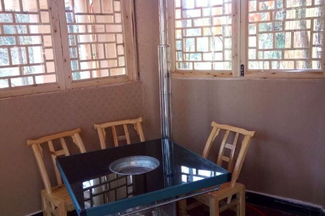 Una habitación con una mesa de vidrio y dos sillas de madera, ventanas amplias con marcos de madera y un radiador en el suelo.