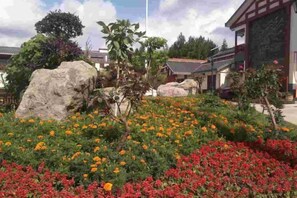 Een tuin met grote rotsen en kleurrijke bloemen, een traditioneel gebouw met een schuin dak en een heldere lucht.