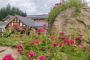 Een klassiek gebouw met pannendak, omgeven door een tuin met roze bloemen.
