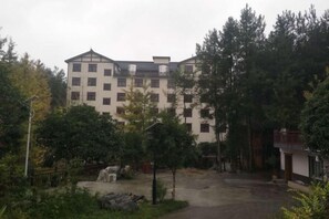 Un immeuble à plusieurs étages, doté d’une façade symétrique, entouré d’arbres et bordé d’une zone pavée.