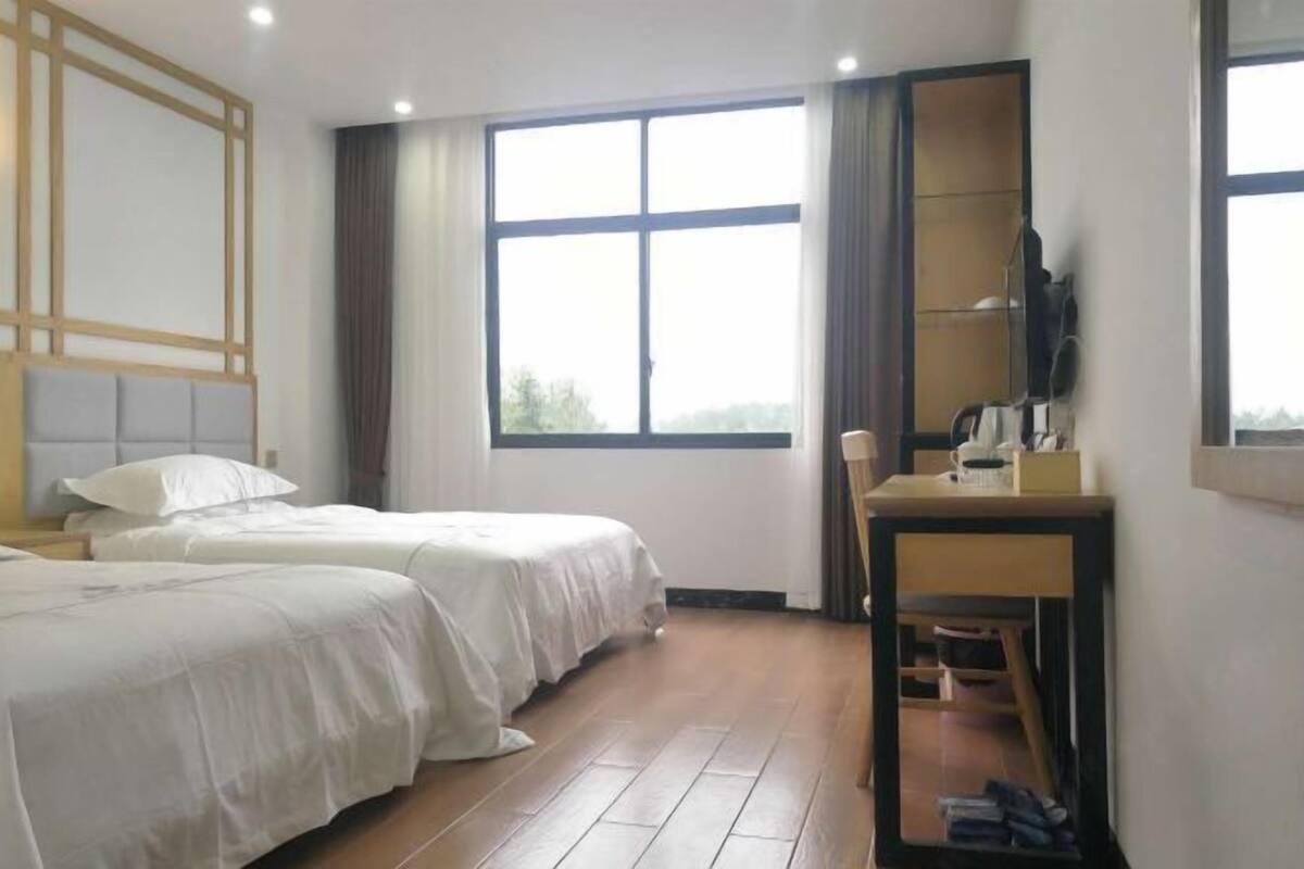 Habitación de hotel con dos camas, un escritorio, una silla, un televisor y un ventanal grande.