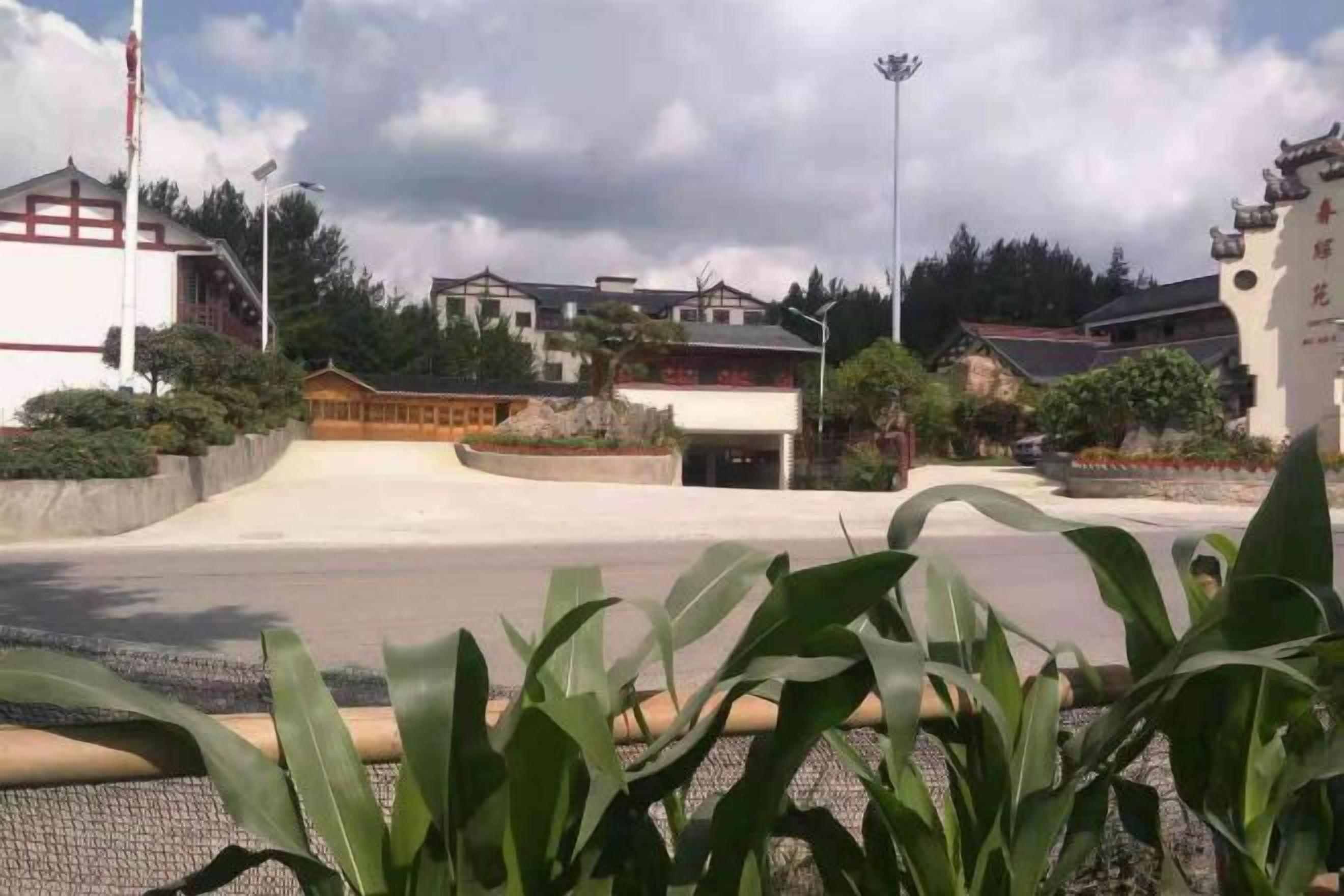 A parking lot with a building in the background, surrounded by greenery.