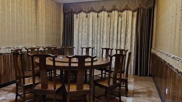 A dining area with a round table surrounded by chairs, a chandelier, and patterned curtains.