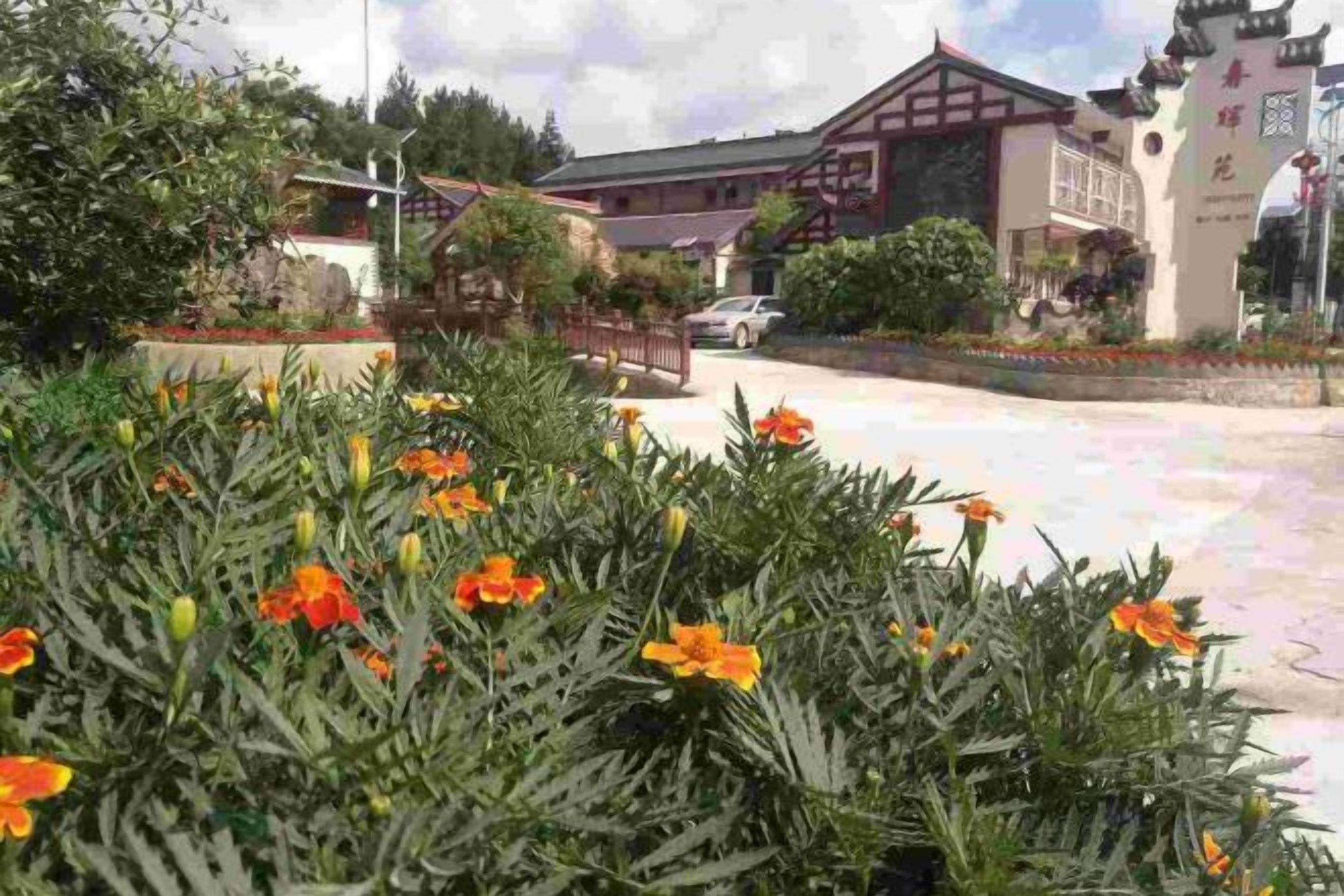 A building with traditional architecture, a paved courtyard, and a garden with flowering plants.