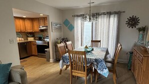 A dining area with a table set for six, surrounded by wooden chairs. A kitchen is visible in the background with wooden cabinets and a built-in oven. - Charming 3-bedroom house in North Myrtle Beach with AC, WiFi, pool and hot tub (North Myrtle Beach)