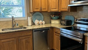 A kitchen with wooden cabinets, stainless steel appliances, a dishwasher, and a window with blinds. - Charming 3-bedroom house in North Myrtle Beach with AC, WiFi, pool and hot tub (North Myrtle Beach)