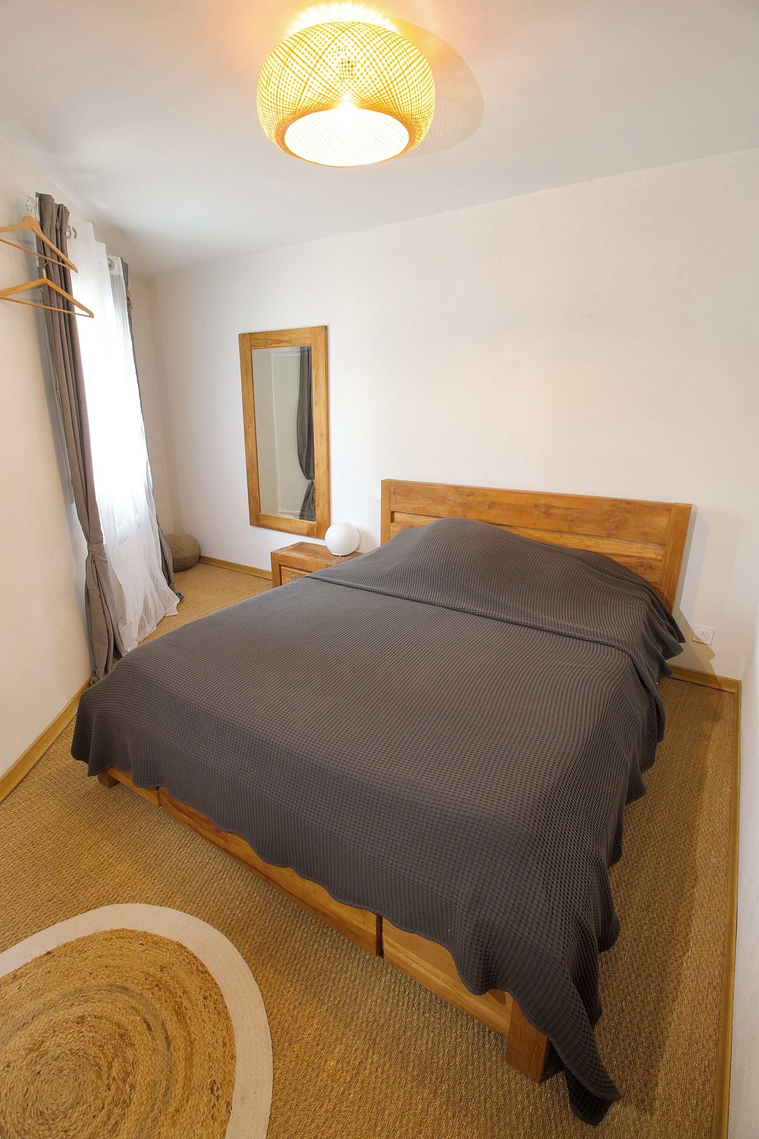 Une chambre à coucher avec un lit en bois, une table de chevet, un miroir et un luminaire suspendu.