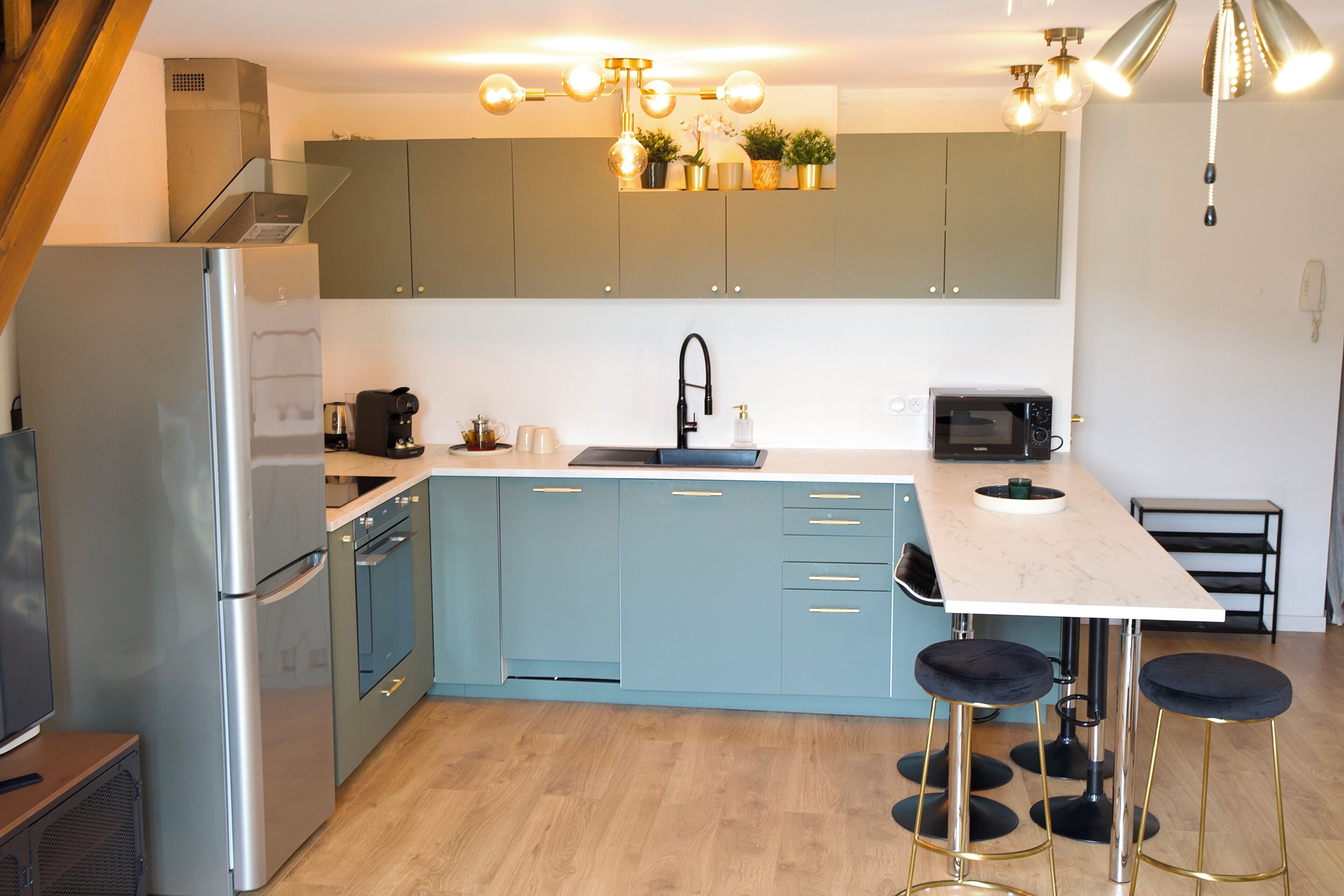 Eine moderne Küche mit einem Edelstahlkühlschrank, einer Mikrowelle und einem Spülbecken. An der Kücheninsel stehen zwei Hocker.