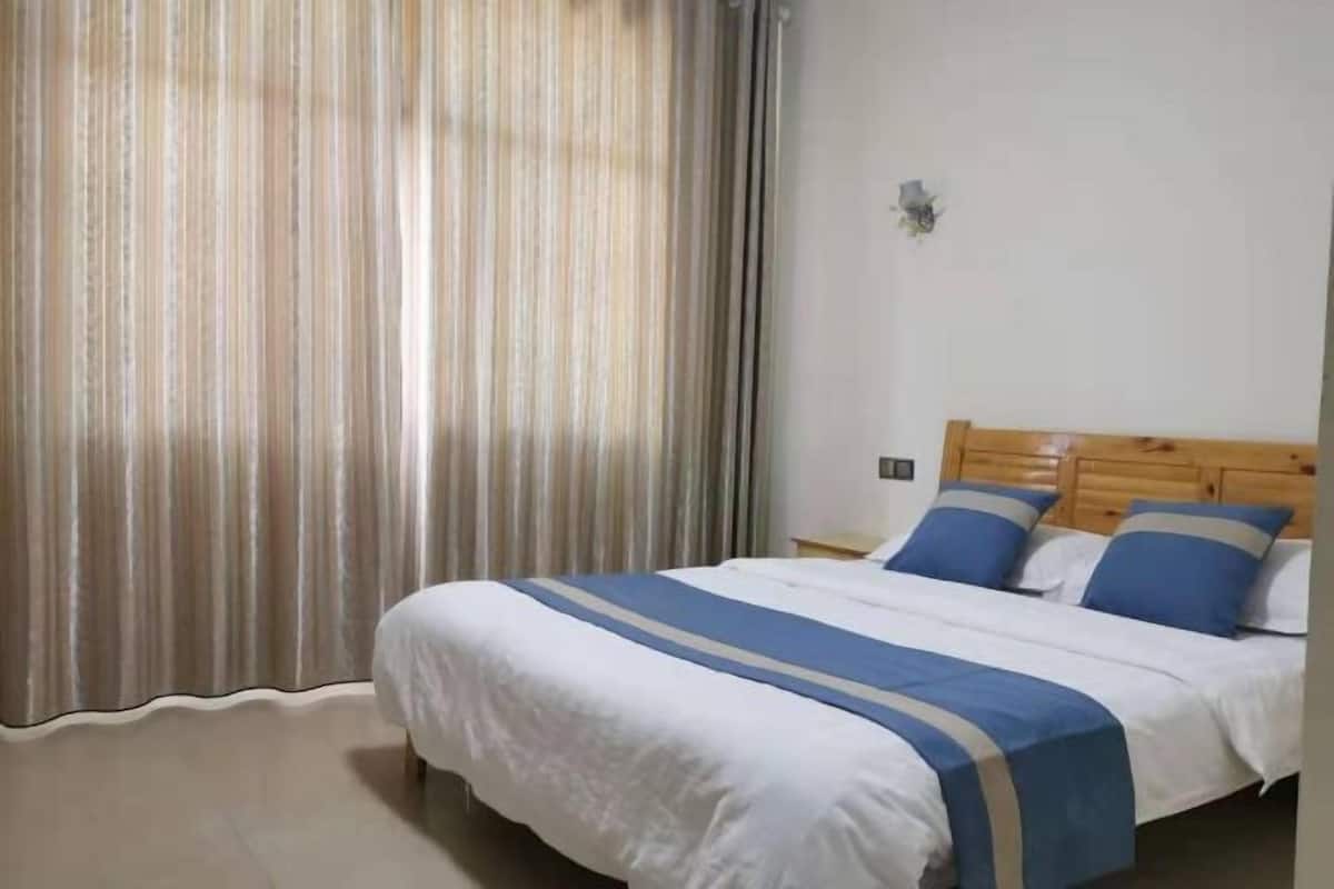 Ein Schlafzimmer mit Bett, Vorhängen, einem hölzernen Kopfteil und einer Wandleuchte.