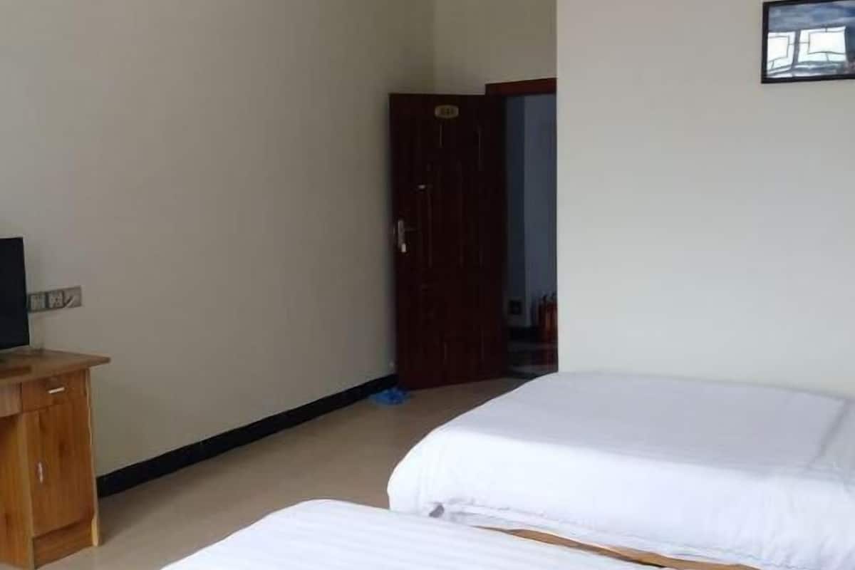 Ein Hotelzimmer mit zwei Betten, einem Holznachttisch, einem Fernseher und einer Tür zu einem weiteren Raum.