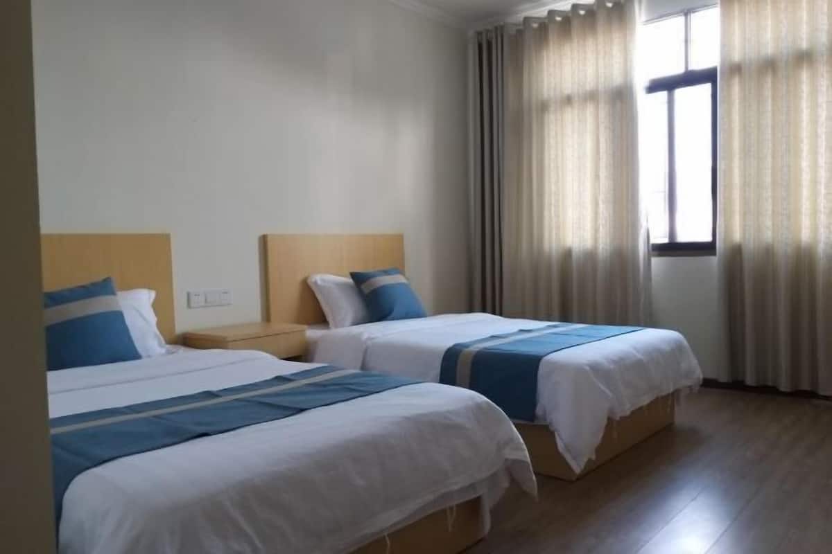 Ein Hotelzimmer mit zwei Betten, Holzboden, einem Fenster mit Vorhängen und einem Nachttisch mit Lampe.