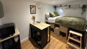 A compact bedroom with a bed, a desk, a TV, and a shelf with decorative items.