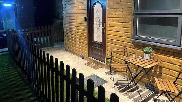 A wooden cabin with a dark wooden door, a window, and a small table with a plant.