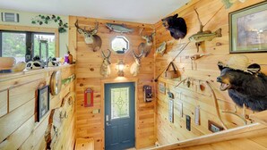Ein Blockhaus-Interieur mit Holzwänden, einer zentralen Tür und verschiedenen aufgehängten Tierköpfen und Fischen.