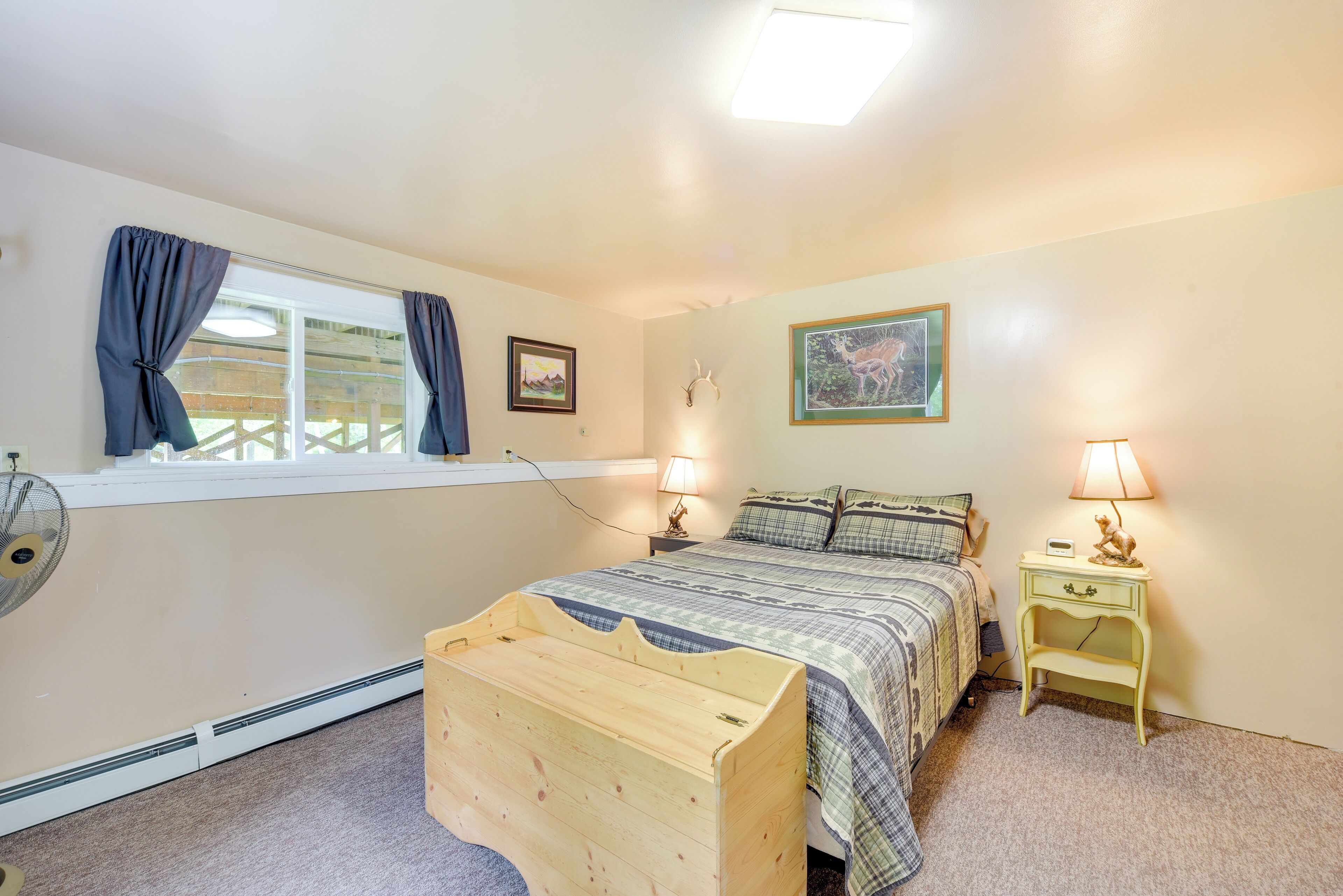 Een slaapkamer met een bed, nachtkastjes, een houten kist, een raam met gordijnen en wandlampen.