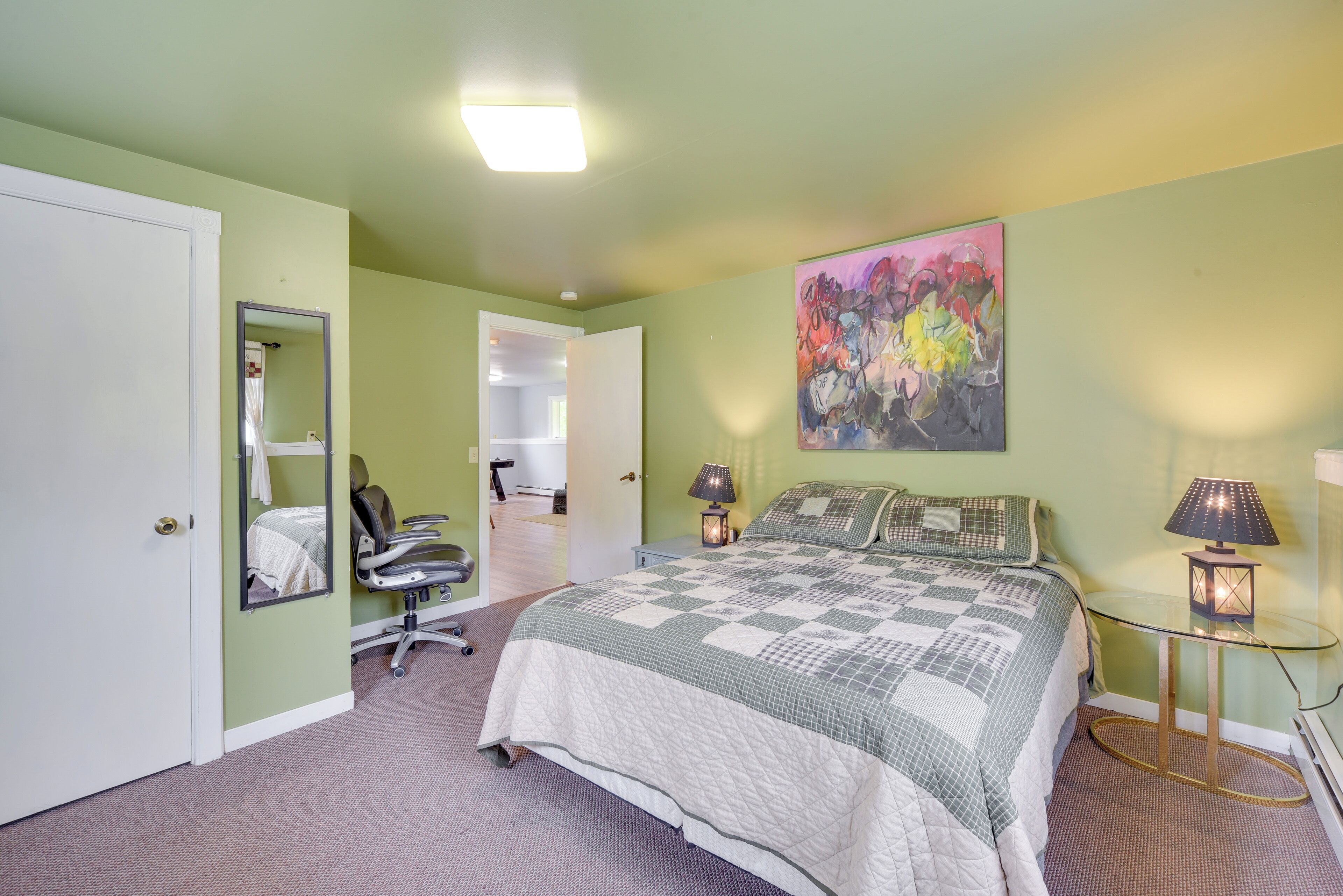 A bedroom with a bed, a chair, a desk, a lamp, and a painting on the wall.