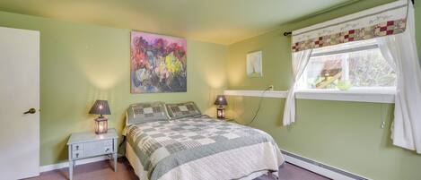 Un dormitorio con cama, mesitas de noche, lámpara, un cuadro y ventana con cortinas.