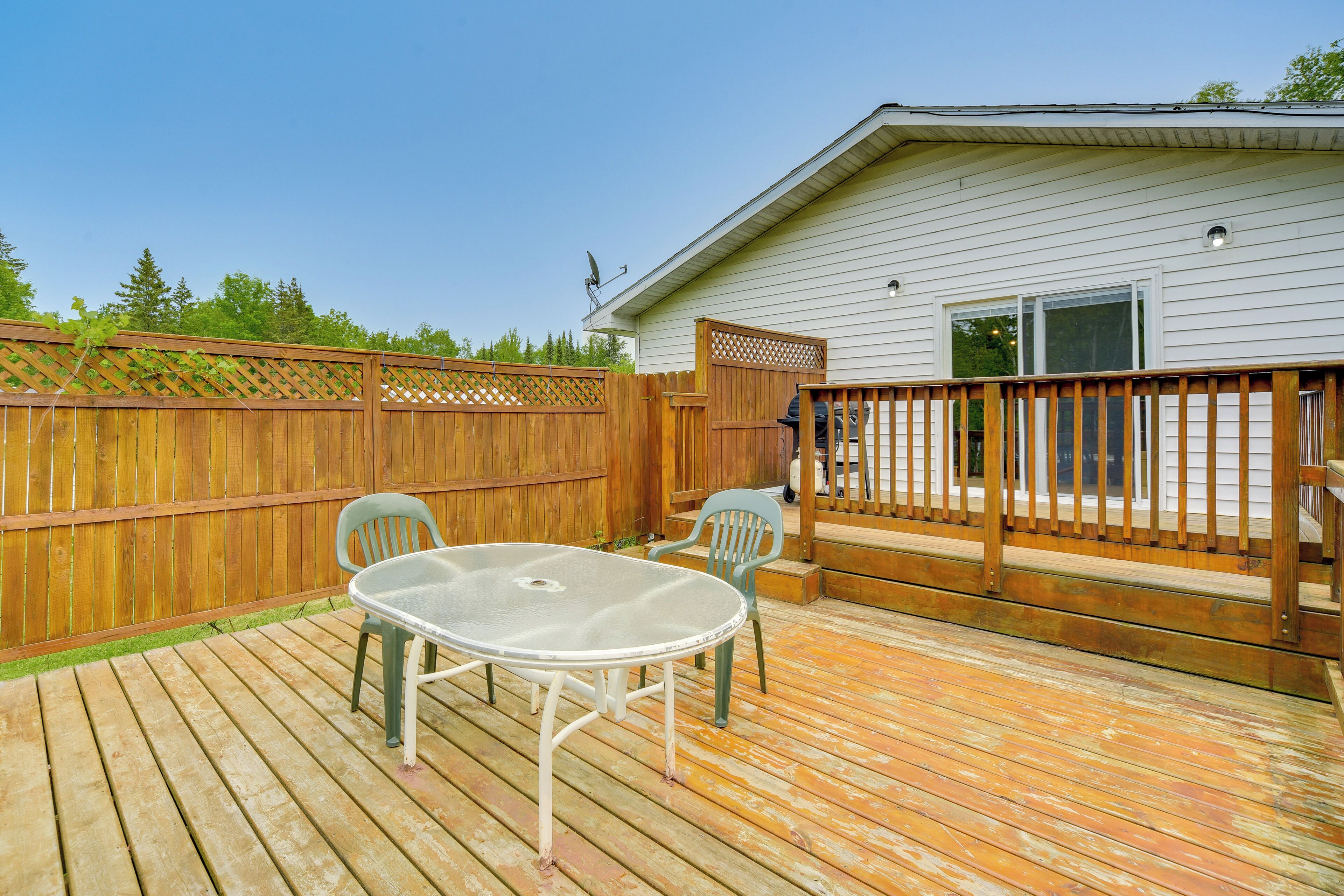 A wooden deck with a table and chairs, a wooden fence, and a house with a window and a door.