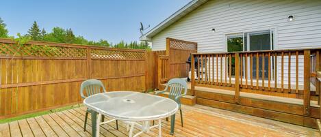 A wooden deck with a table and chairs, a wooden fence, and a house with a window and a door.