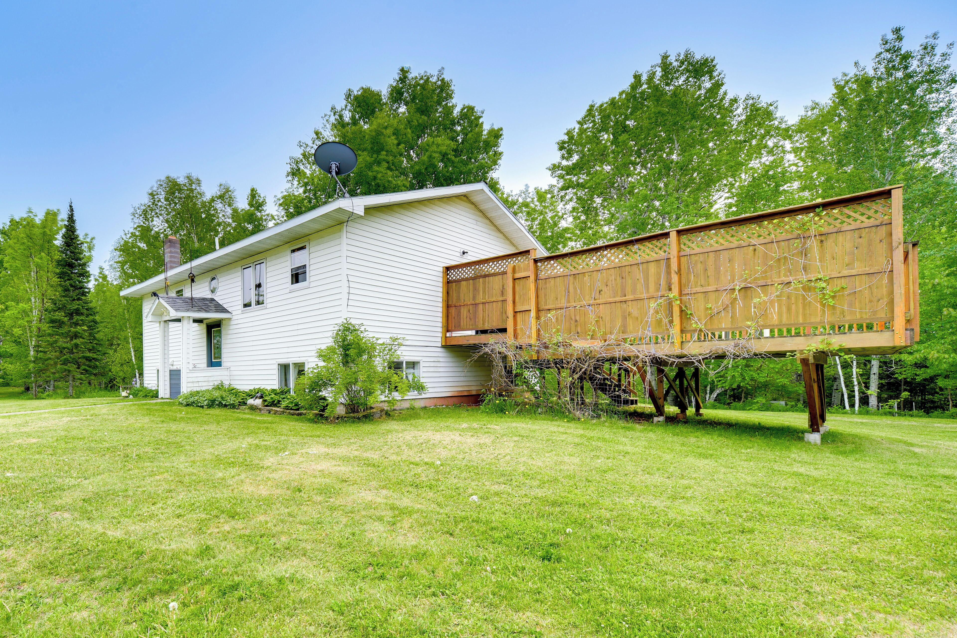 A white house with a satellite dish, a wooden deck, and a lush green lawn.