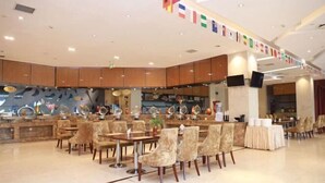 A spacious restaurant with multiple dining tables and chairs, a long counter with a variety of items, and a ceiling decorated with flags. - Mingdu Hoki International Hotel (Changzhou)