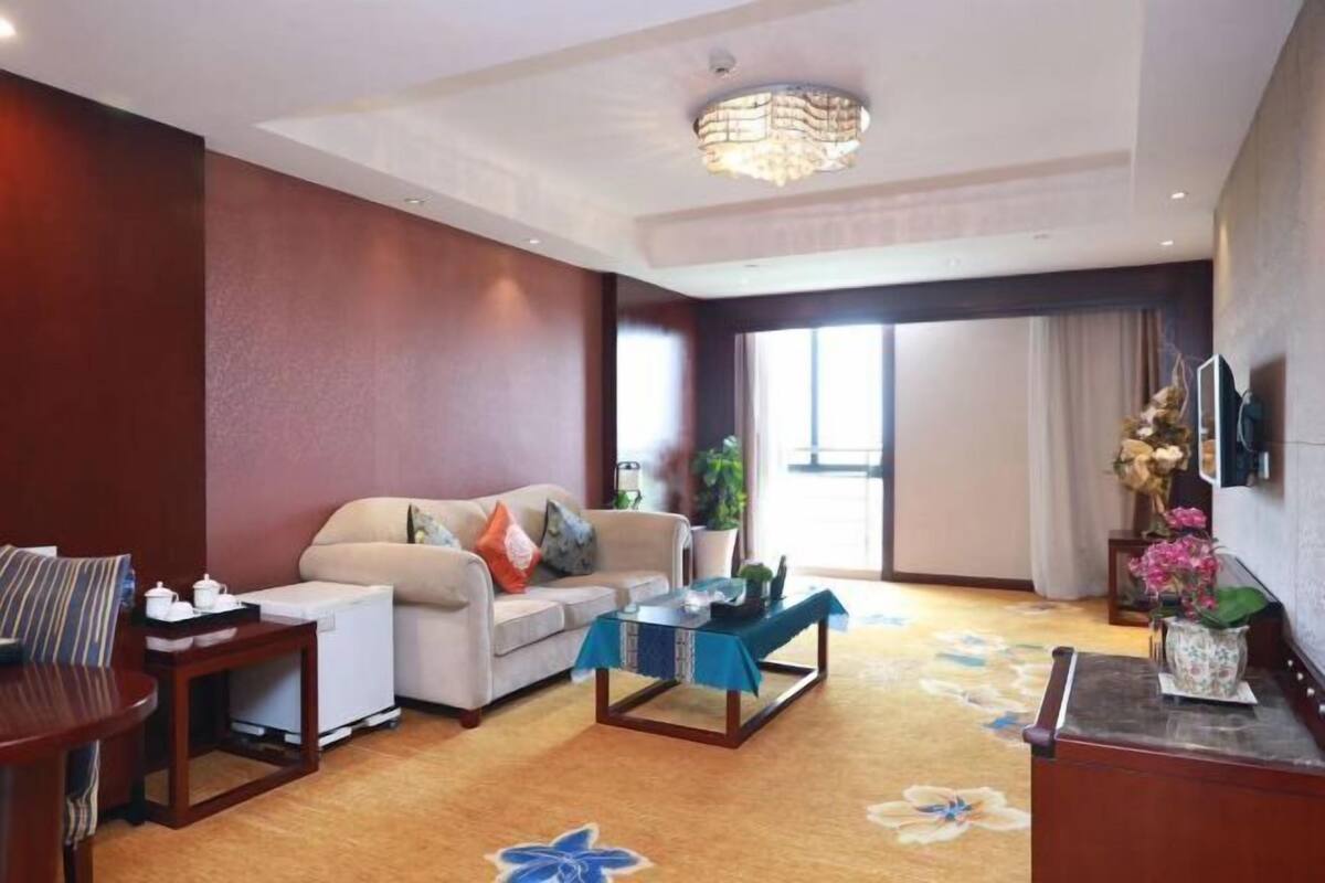 A hotel room with a sofa, a coffee table, a TV, and a large window.