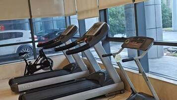 A gym with treadmills and a stationary bike, large windows, and a view of the outside.