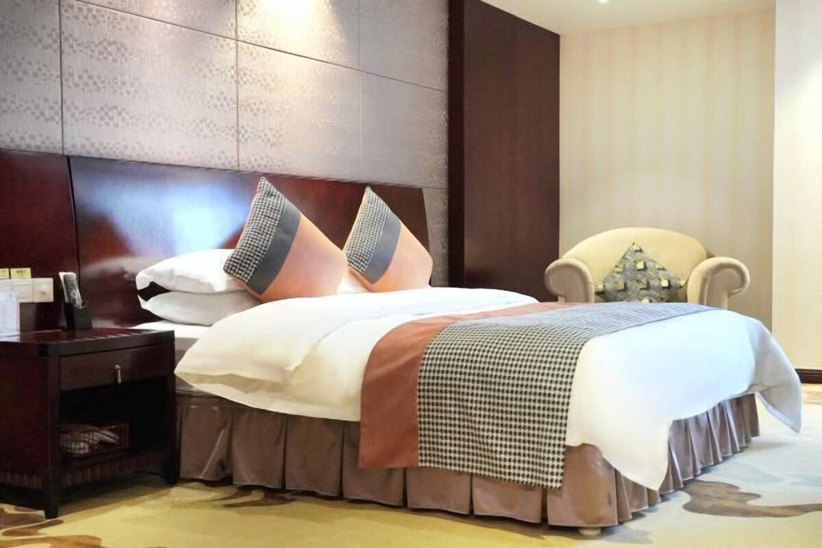 A hotel room with a large bed, a nightstand, a chair, and a headboard with a patterned design.