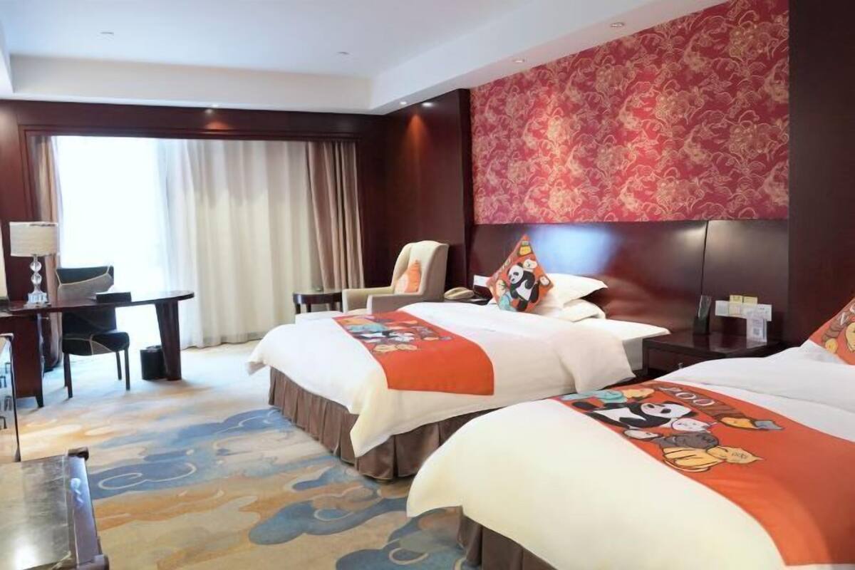 A hotel room with two beds, a desk, a chair, and a large window with curtains.