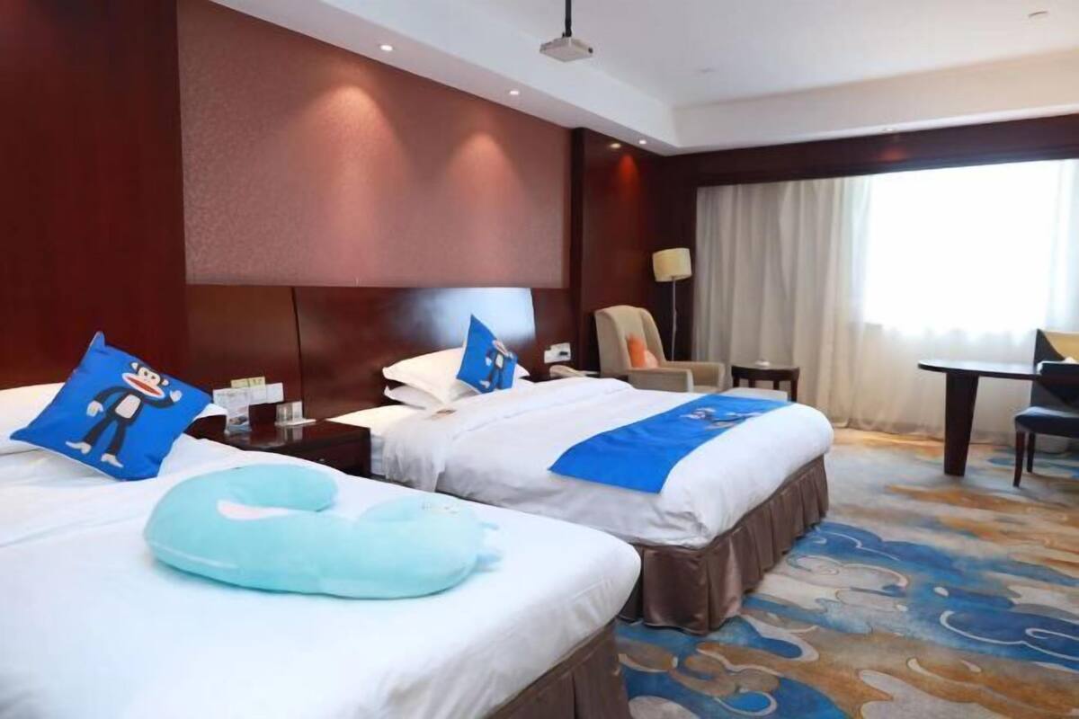 A hotel room with two beds, a desk, a chair, and a large window with curtains.