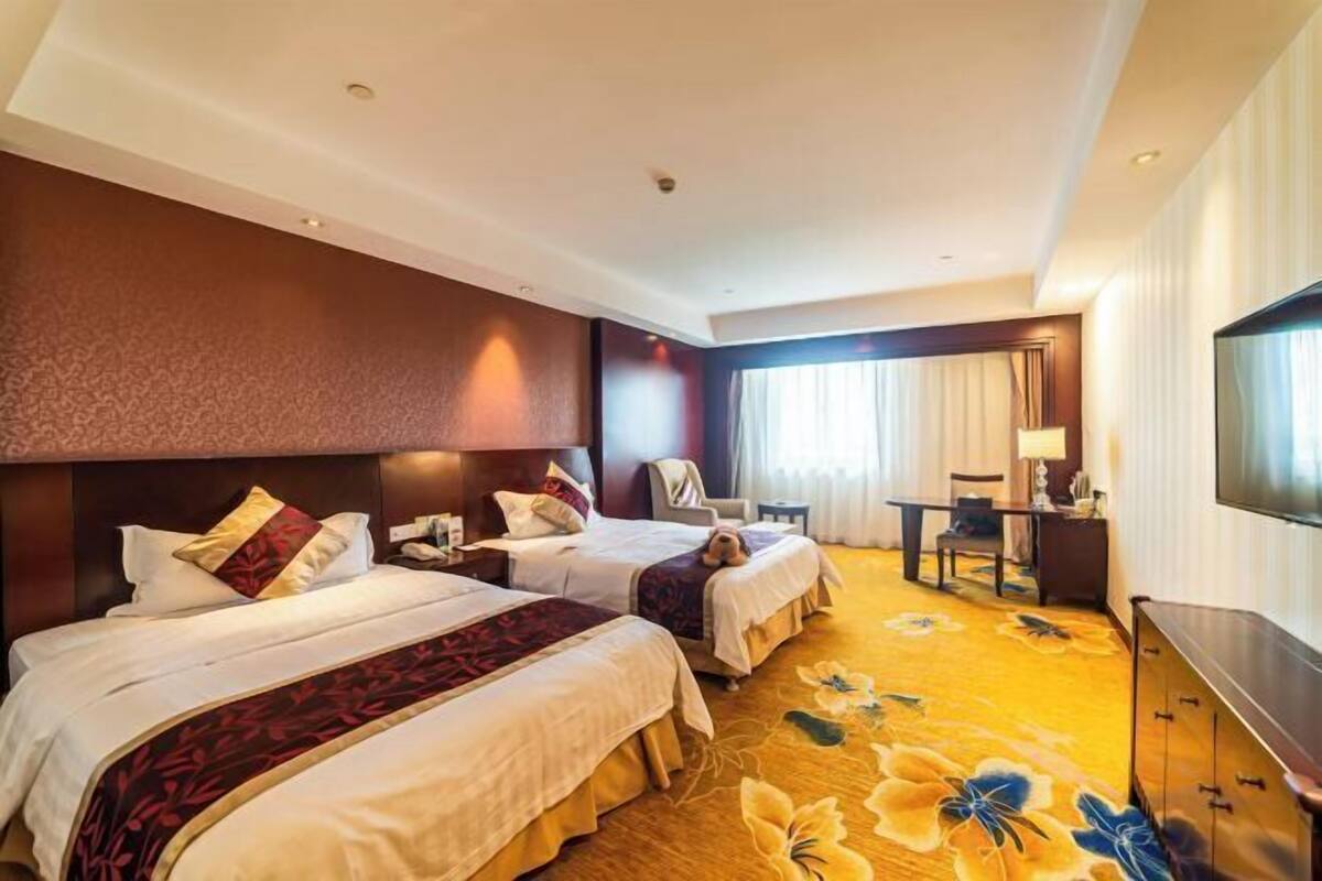 A hotel room with two beds, a desk, a chair, a TV, and a carpet with floral design.
