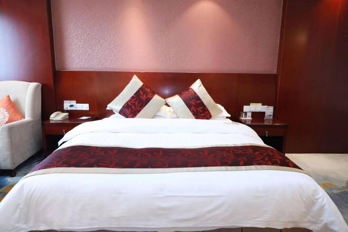 A hotel room with a large bed, a nightstand, a chair, and a wall-mounted telephone.