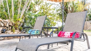 Two outdoor lounge chairs with metal frames and grey fabric, positioned on a stone patio with a thatched roof overhead. - Grotto Pool House: Premium 3-Bed Villa w/ Private Pool, 5 Min to IMG (Bradenton)