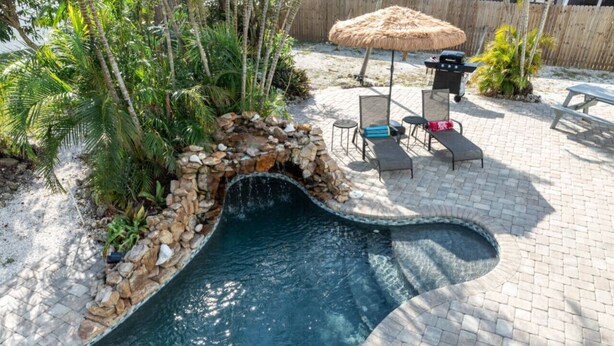A swimming pool with a stone waterfall feature, surrounded by a brick patio and tropical plants. - Grotto Pool House: Premium 3-Bed Villa w/ Private Pool, 5 Min to IMG (Bradenton)