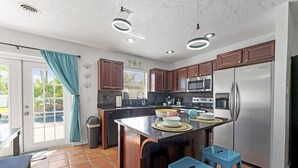 A modern kitchen with a central island, stainless steel appliances, and a sliding glass door leading to a patio. - Grotto Pool House: Premium 3-Bed Villa w/ Private Pool, 5 Min to IMG (Bradenton)