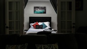 A hotel room with a bed, a painting above the bed, and a view through an open door. - Grotto Pool House: Premium 3-Bed Villa w/ Private Pool, 5 Min to IMG (Bradenton)