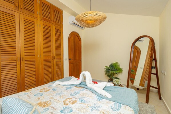 A bedroom with a bed, wooden wardrobe, a mirror, and a hanging light fixture.