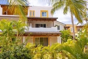 Edificio de dos pisos con balcón, rodeado de exuberante vegetación tropical.