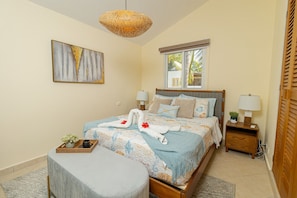 A neatly arranged bedroom with a bed, bedside tables, a hanging light fixture, a window, and a painting on the wall. - Charming 1BR in Dominicus w Pool (Dominicus)