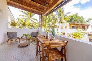 A balcony with wooden furniture, potted plants, and a view of palm trees and buildings. - Charming 1BR in Dominicus w Pool (Dominicus)