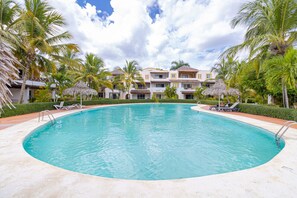 A large, clear swimming pool surrounded by palm trees and a building with multiple balconies. - Charming 1BR in Dominicus w Pool (Dominicus)