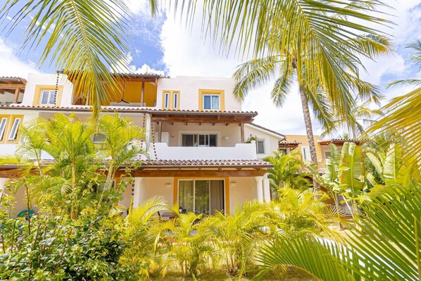 Un immeuble à plusieurs étages doté d’un balcon, entouré d’une végétation tropicale luxuriante.