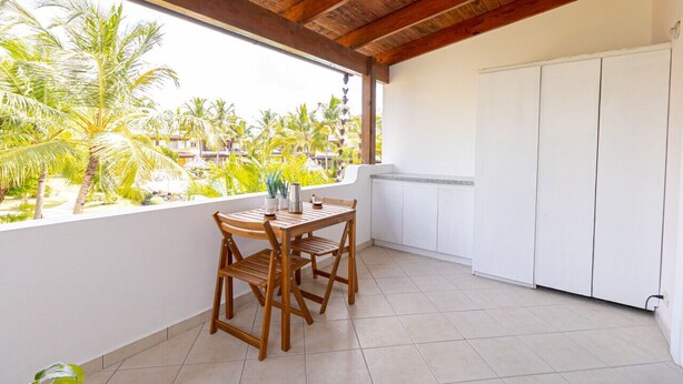 Un balcon avec une table et des chaises en bois, un meuble blanc et une vue sur des palmiers et des immeubles.