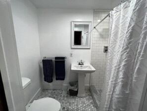 Une petite salle de bain compacte, avec des toilettes blanches, un lavabo et un espace douche.