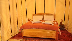 Ein Bett mit Holzrahmen und orangefarbener Bettwäsche, vor einer gelben, zeltartigen Struktur mit schwarzer Zierleiste.