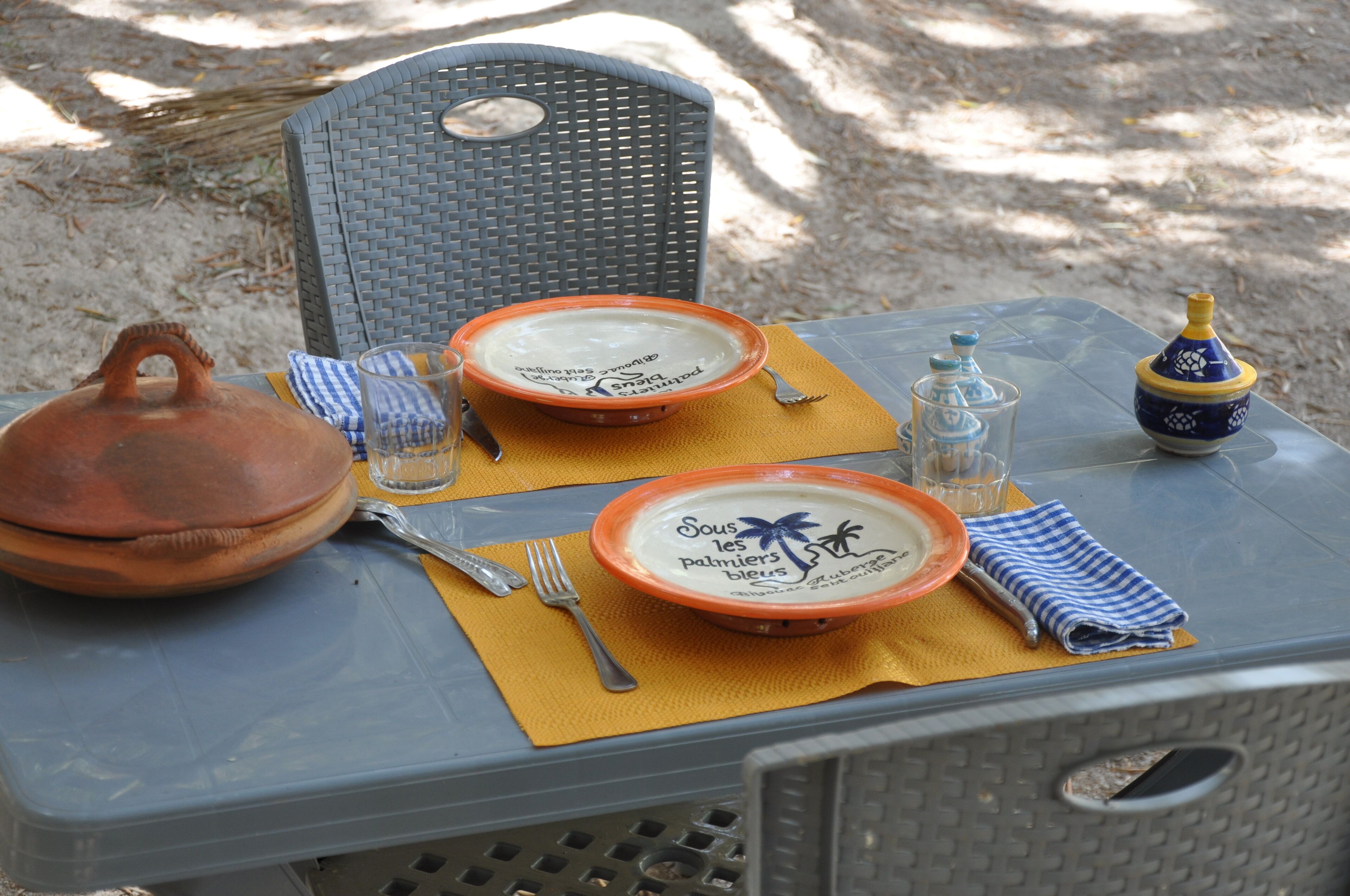 A table set with plates, a teapot, and a bottle, placed on a chair outdoors.