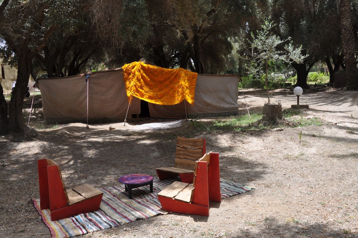 Un camping con una tienda de campaña, una mesa de picnic y dos sillas rojas.