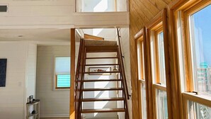 A spacious room with a wooden staircase leading to a loft area, large windows, and a view of the city. -  Hatteras House  (Hatteras)