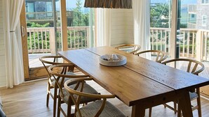 A spacious dining area with a wooden table and chairs, large windows offering a view of the outdoors, and a ceiling light fixture. -  Hatteras House  (Hatteras)